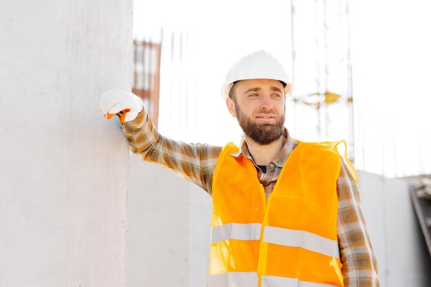 Bouwer, reparateur, voorman in veiligheidshelm en vest werkt op zijn werkplaats in een gebouw dat in aanbouw is