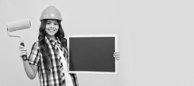 Bouwer tienermeisje in helm gelukkig kind met krullend haar in helm houd verfroller en school