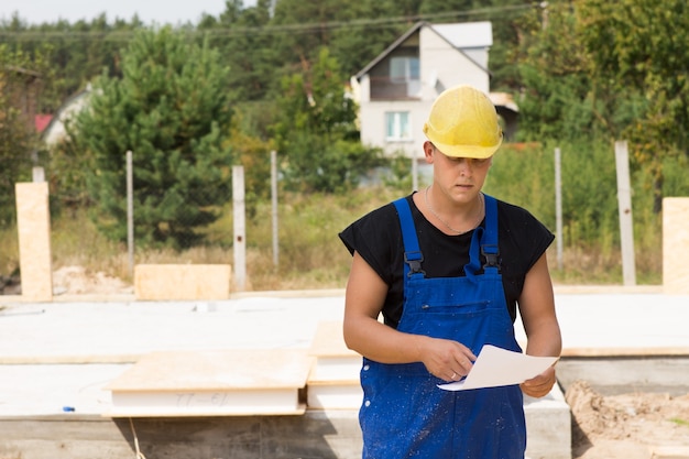 Bouwers die specificaties of een bestelling van bouwmaterialen controleren terwijl hij ter plaatse staat in zijn veiligheidshelm en overall