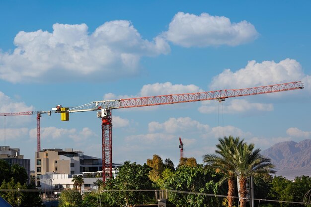 Foto bouwkranen boven het onvoltooide woongebouw tegen een wolkenhemel grote bouwplaats met twee kranen die werken aan een bouwcomplex met palmbomen in het stadslandschap