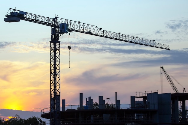 Bouwkranen met gebouwde huizen op het oppervlak van de avondrood