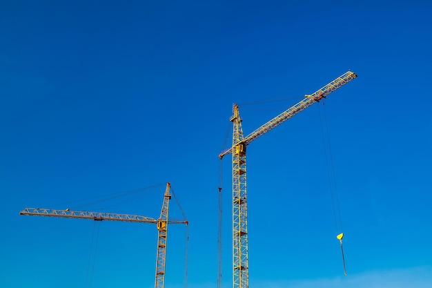 Bouwkranen werken op de creatieplaats tegen de blauwe hemelachtergrond Onderaanzicht van industriële kraan Concept van de bouw van appartementsgebouwen en renovatie van woningen Kopieer ruimte