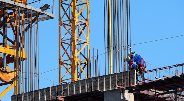 Bouwplaats en arbeid werken aan hoog gebouw dat rond met metaal en betonmateriaal is en risico's in hun leven loopt.