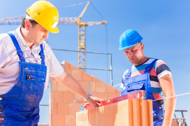 bouwplaatsmedewerker of metselaar met helmen die muren besturen met een waterpas of bouwen of leggen of metselen van muur op gebouw