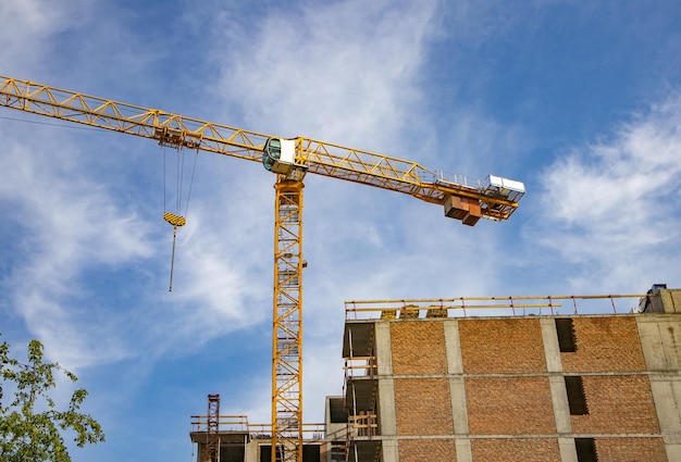 Bouwtorenkraan op de bouwplaats van een modern bakstenen woongebouw tegen de achtergrond van de zomer van de zonlichtzonsopgang