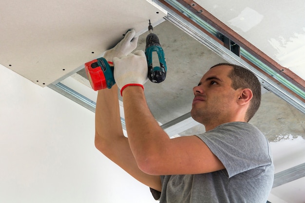 Bouwvakker assembleert een verlaagd plafond met gipsplaten en het bevestigen van de gipsplaten aan het plafond metalen frame met schroevendraaier.