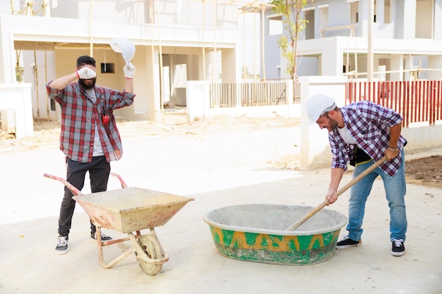 Bouwvakker die beschermende handschoenen en veiligheidshelm draagt, mengt cement om op de bouwplaats te bouwen