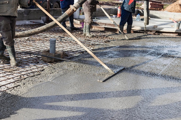 Bouwvakker die een gegoten betonnen vloer egaliseert in een industriële werkplaats. Benen in laarzen in beton. Oppervlakte betonneren. Monolithische gewapend beton werken.