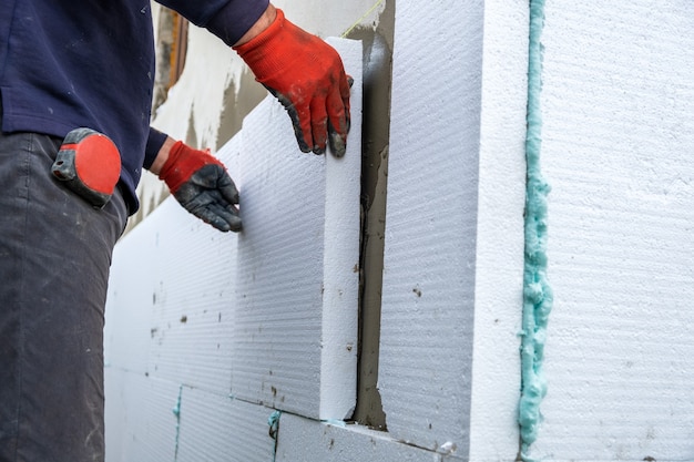 Bouwvakker die styrofoam-isolatieplaten op de muur van de huisgevel installeert voor thermische bescherming.