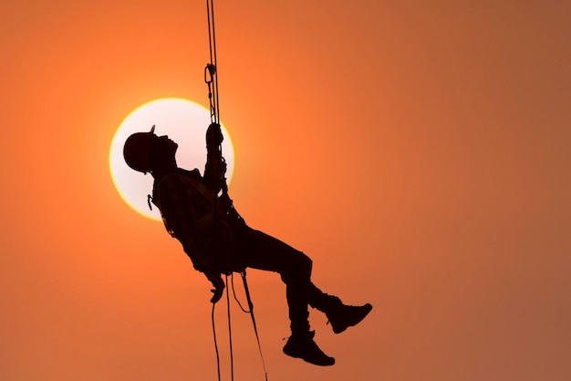 Foto bouwvakker die veiligheidswerk draagt bij hoog uniform op steigers op de bouwplaats tijdens zonsondergang, werken op hoogteapparatuur.