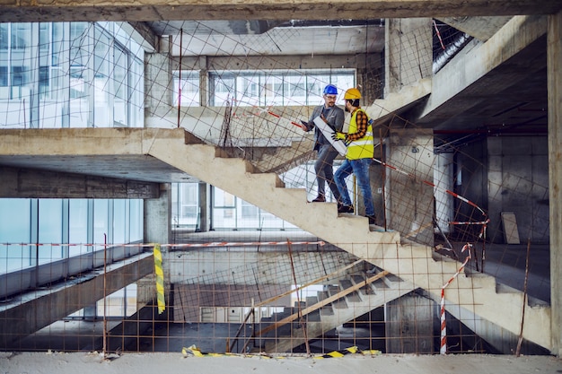 Bouwvakker en hoofdarchitect die de trap oplopen en praten over de voortgang bij de bouw van een nieuw gebouw.