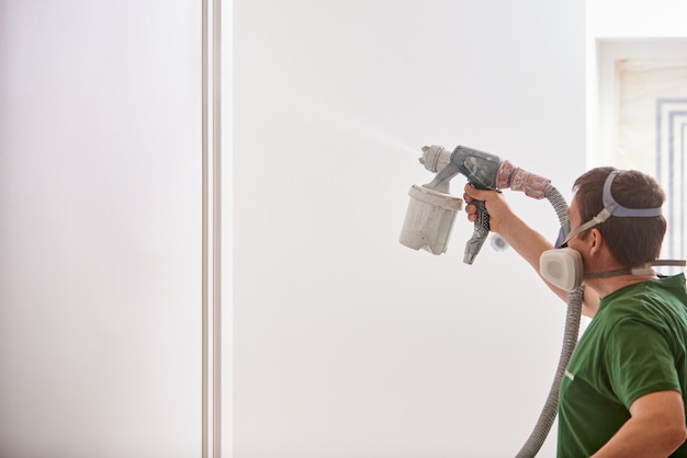 Bouwvakker schilderende muur met spuitpistool in witte kleur