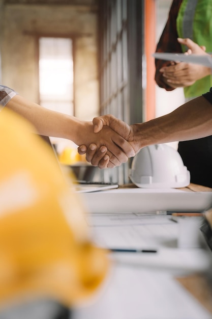 Bouwvakkers architecten en ingenieurs schudden elkaar de hand terwijl ze werken aan teamwerk en samenwerking na het voltooien van een overeenkomst in een succesvol samenwerkingsconcept voor kantoorfaciliteiten