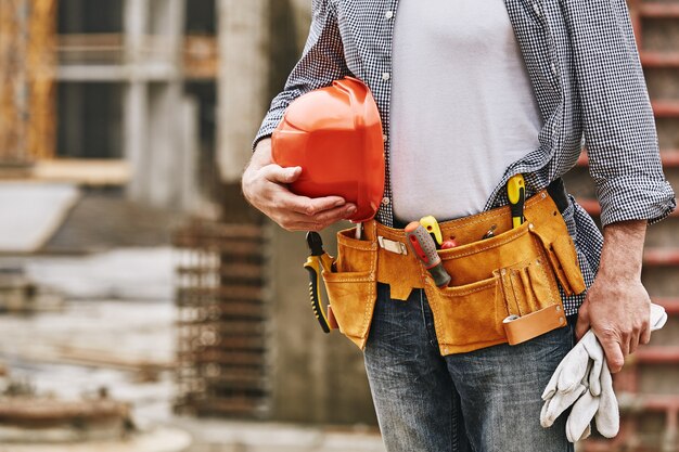 Bouwveiligheid bijgesneden afbeelding van mannelijke bouwer met helm en gereedschapsriem die in de bouw werkt