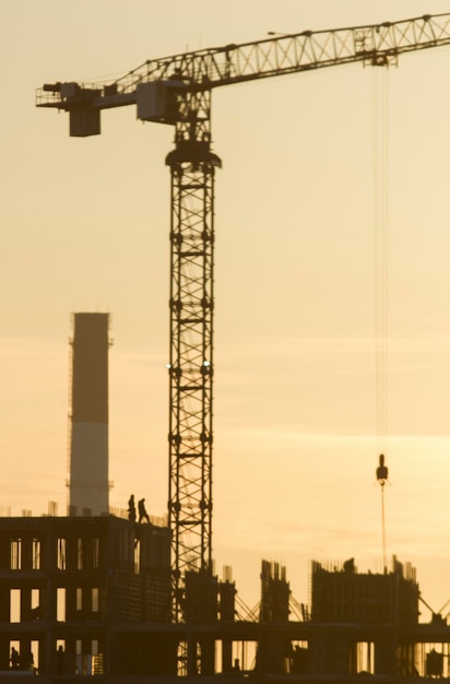 Bouwzijde - silhouet bij zonsondergang - arbeiders, kranen - onafgewerkt gebouw, telefoto