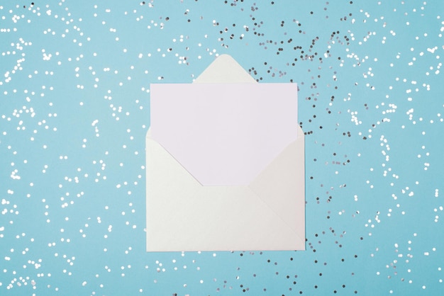 Boven boven plat lag close-up foto van open witte envelop en vel papier op lichte pastelblauwe achtergrond met zilveren confetti