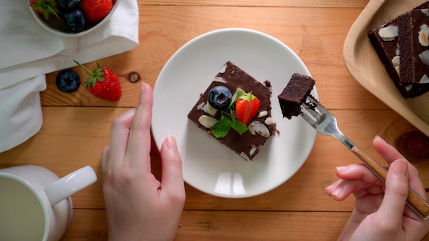 Boven geschoten van een vrouw die chocoladebrownie op witte plaat eet