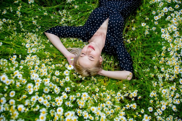 Boven het oog op blonde vrouw in zwarte jurk liggend in platteland chamomiles bloemen weide