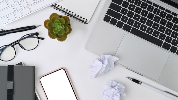 Boven weergave rommelige werkruimte met laptopcomputer, smartphone, notebook en verfrommeld papier.