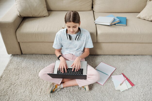 Boven weergave van geconcentreerde tienermeisje zittend op een tapijt en met behulp van laptop tijdens het leren van les