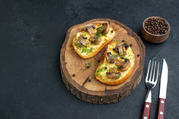 Boven weergave van heerlijke snack met champignons op een houten bord en bestekset peper op zwarte achtergrond