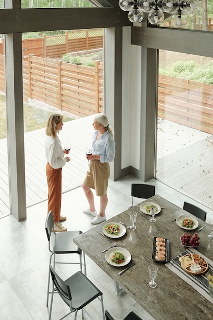 Boven weergave van jonge dochter en senior moeder permanent in moderne keuken van cottage huis en wijn drinken tijdens het chatten