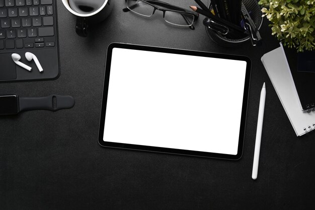 Boven weergave van moderne donkere werkplek met digitale tablet, styluspen, oortelefoon en slim horloge op zwart leer.