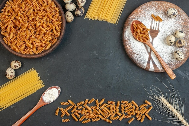 Boven weergave van vrije ruimte tussen rauwe pasta's meel eieren en spikes vork mes getekend met bloem op snijplank op zwarte achtergrond