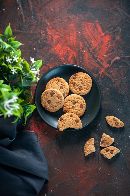 Boven weergave van zelfgemaakte heerlijke suikerkoekjes op zwarte plaat en bloempot op donkere achtergrond van mixkleuren