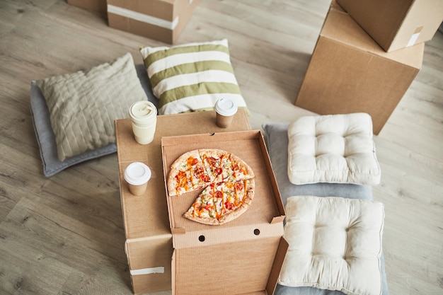 Bovenaanzicht achtergrondafbeelding van pizza op kartonnen doos als geïmproviseerde tafel in lege kamer terwijl familiemo...