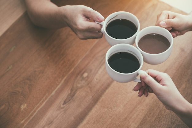 Bovenaanzicht afbeelding van drie mensen rammelende koffiekopjes op houten tafel in café