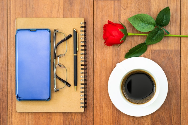 Bovenaanzicht afbeelding van koffiekopje, notebook en mobiel met oogglas op houten tafel achtergrond voor het toevoegen van tekst of mockup