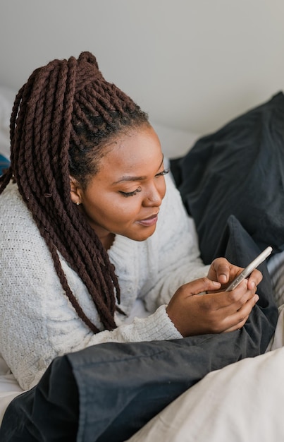 Bovenaanzicht Afro-Amerikaanse vrouwelijke student gekleed terloops mobiele telefoon vasthouden en berichten typen en communiceren met vrienden via sociale netwerken met behulp van een hoge internetverbinding