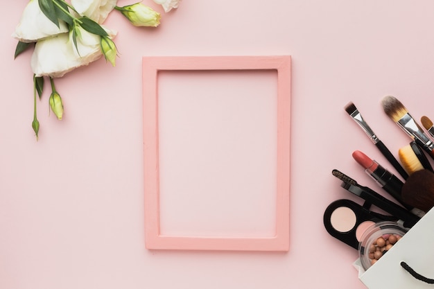 Foto bovenaanzicht arrangement met roze frame en make-up producten