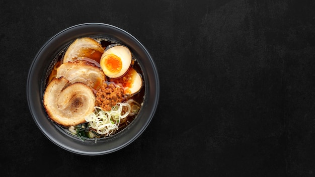 Bovenaanzicht Aziatische ramen noedelsoep met Chashu Japans gestoofd buikspek Nitamago ei gesneden lente-ui Ajitsuke Menma en gedroogd zeewier op donkere textuur achtergrond met kopie ruimte voor tekst