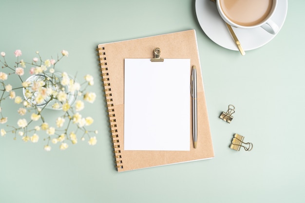 Bovenaanzicht blanco papier Notebook, bloemen, gouden bindmiddelclips, kopje koffie en pen. Plat leggen