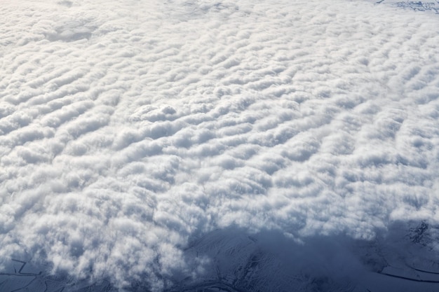 Bovenaanzicht boven wolken vanuit vliegtuigraam, dikke witte blauwe wolken zien eruit als zacht schuim