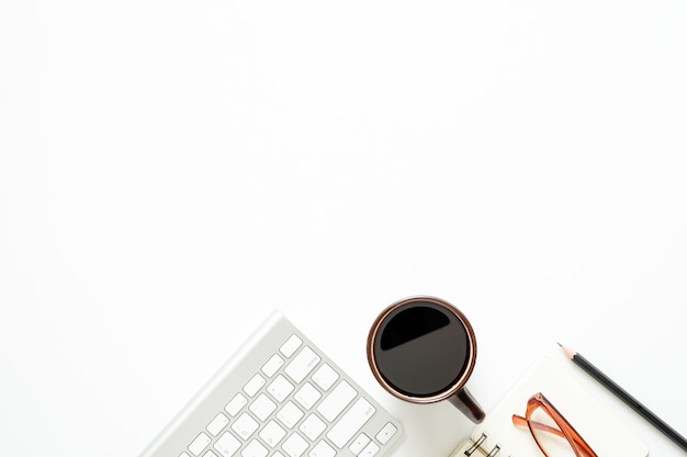 Bovenaanzicht bureau met een computer, potlood, glazen, notebookpapier en een koffiekopje.