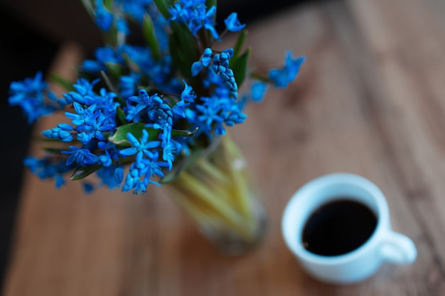 Bovenaanzicht close-up van blauwe viooltjes bloemen op achtergrond van wazig houten tafel in de buurt van kopje koffie.