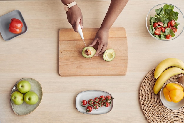 Bovenaanzicht close-up van onherkenbare zwarte vrouw die avocado snijdt tijdens het koken van een gezonde maaltijd in de keuken