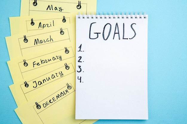 bovenaanzicht doelen geschreven op papier op spiraalvormige notitieboekje maandelijkse herinneringskaarten op blauwe tafel