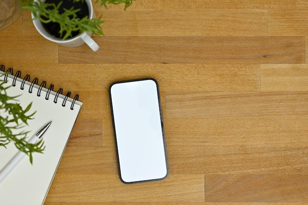 Bovenaanzicht Een smartphonemodel met spiraalvormig notitieblok en koffiekopje op houten tafelblad