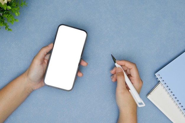 Bovenaanzicht Een vrouwelijke handen met een pen en een smartphonemodel op blauwe achtergrond