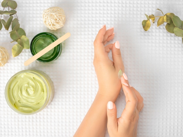 Bovenaanzicht en plat leggen van vrouw met crème op handen over witte handdoek met cosmetische producten - avocado-olie, room en bamboestok. bovenaanzicht