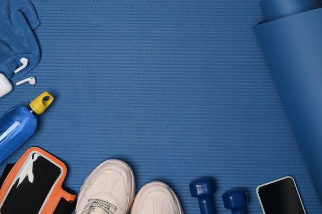 Bovenaanzicht fitnessapparatuur en mobiele telefoon op blauwe mat.