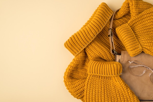 Bovenaanzicht foto van gele pullover lederen tas en stijlvolle bril op geïsoleerde pastel beige achtergrond met copyspace