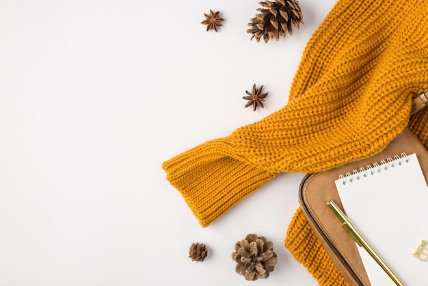 Bovenaanzicht foto van gele trui gouden pen notebook beige lederen tas en dennenappels op geïsoleerde witte achtergrond met copyspace