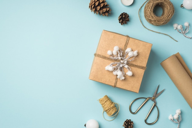 Bovenaanzicht foto van geschenkdoos versierd met sneeuw takje en touw witte kerstboom ballen en dennenappels op geïsoleerde pastel blauwe achtergrond met lege ruimte