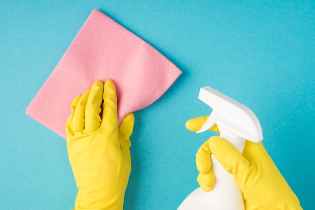 Bovenaanzicht foto van handen in gele rubberen handschoenen met roze viscose vod en witte spuitfles op geïsoleerde pastelblauwe achtergrond