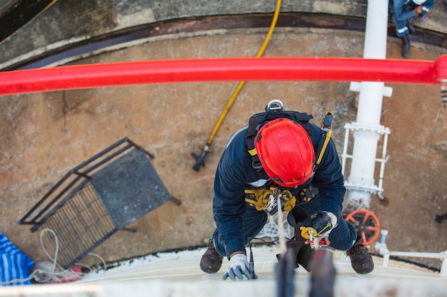 Bovenaanzicht foto van industriële lasser met touwtoegang die op hoogte werkt met een harnas, helm veiligheidsuitrusting touwtoegangsinspectie van de industrie van de dikteopslagtank.